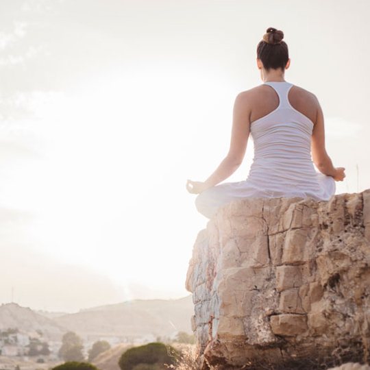 A woman meditating peacefully on a rock at sunrise